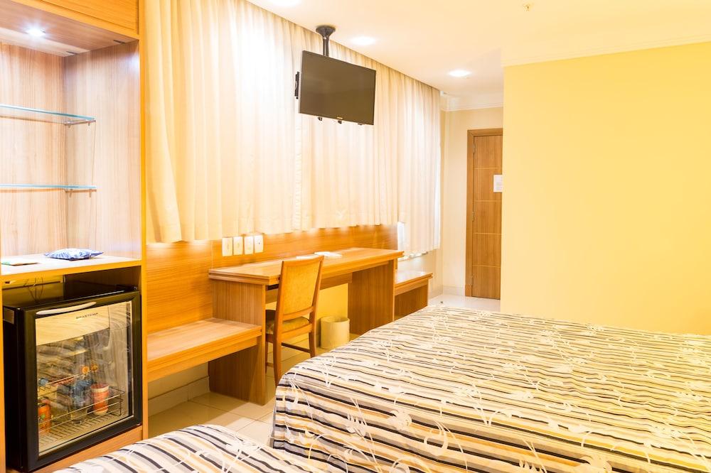 Hotel Atlantico Business Centro Rio de Janeiro Exterior photo The photo shows a hotel room with two beds featuring striped bedding. There is a wooden desk and chair near a window with light-colored curtains. A flat-screen television is mounted on the wall, and there appears to be a small refrigerator or mini-ba